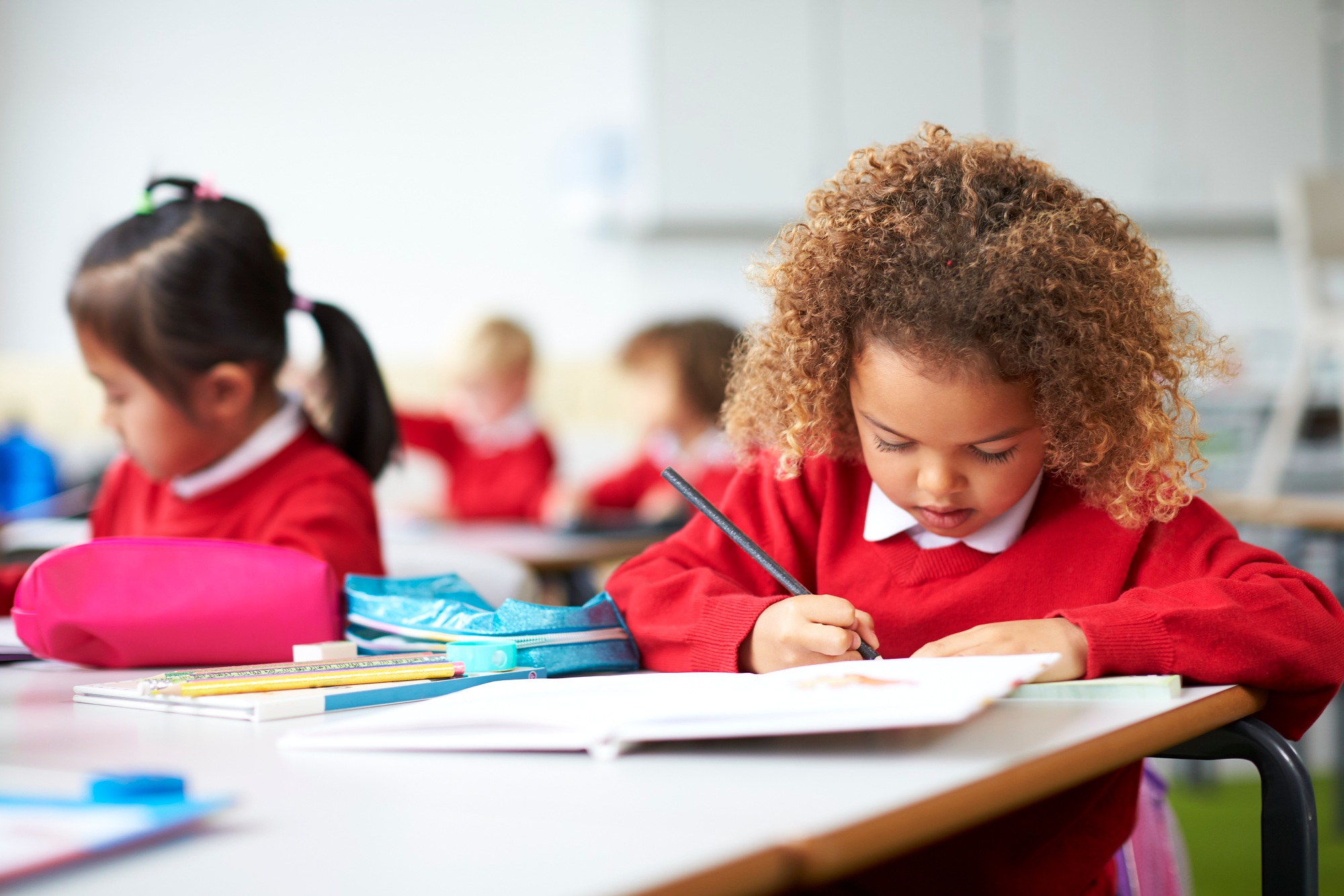 Schoolgirl sitting at a desk in an infant school classroom drawing, close up